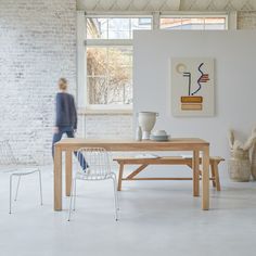 a woman walking past a wooden table in a white room