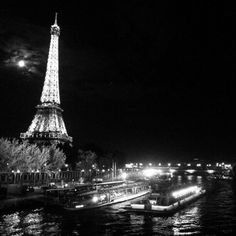 the eiffel tower lit up at night with boats on the river below it