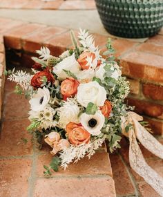 a bridal bouquet sitting on top of a brick floor next to a potted plant