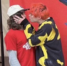 two people standing next to each other with orange hair and one wearing a red shirt