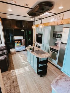 a kitchen and living room inside of a mobile home with wood flooring, blue cabinets, stainless steel appliances and an island in the middle