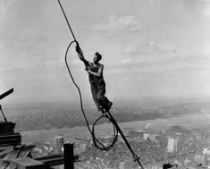 a black and white photo of a man on top of a building holding onto a rope