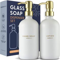 two white soap bottles with gold caps are in front of a blue box that says, glass soap dispenser set