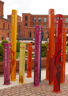 several tall colorful poles on the side of a brick walkway in front of a building