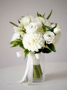 a vase filled with white flowers on top of a table next to a ribbon tied around it