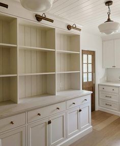 an empty kitchen with white cabinets and wood flooring on the walls, along with hanging lights