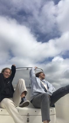 two people sitting on the back of a boat with their arms up in the air