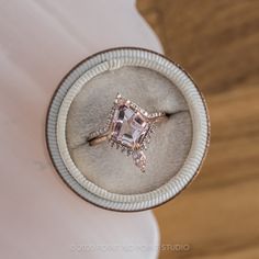 an engagement ring with a pink diamond surrounded by white diamonds in a box on top of a wooden table