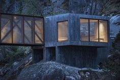 a house built on top of a rock in the woods at night with light coming from windows