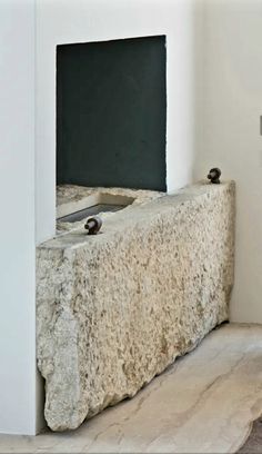 a stone fountain in the corner of a room with white walls and floor tiles on it