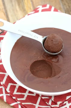 a spoon with chocolate in it on a red and white towel next to a bowl