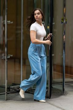 a woman in white shirt and blue pants walking by glass doors with her hair blowing in the wind