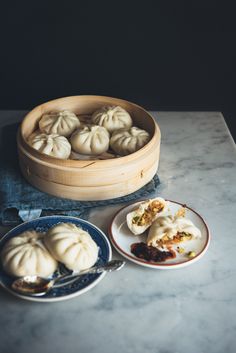 several plates with dumplings in them sitting on a marble countertop next to a wooden steamer