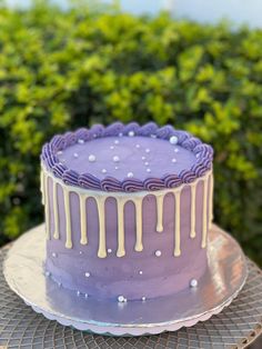 a purple cake sitting on top of a metal platter next to green bushes and shrubbery