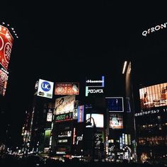 the city is lit up at night with neon signs and billboards on it's buildings