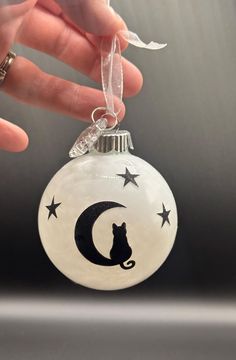 a hand holding a glass ornament with a cat on the moon and stars