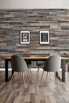 two gray chairs sitting at a wooden table in front of a wall with wood planks