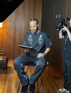 a man sitting in a chair while holding a tablet next to another man with a camera