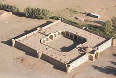 an aerial view of a large building in the middle of a dirt field with trees