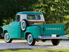 an old green truck is parked on the side of the road in front of some trees