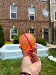 a hand is holding an orange ball in front of a brick building with a pool