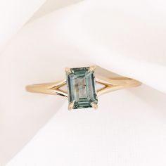 a ring with an emerald colored stone on it sitting on a white cloth covered surface