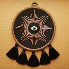 an embroidered wall hanging with black tassels and a green eye in the center