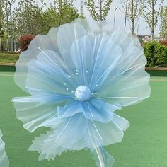 a large blue flower sitting on top of a green tennis court covered in plastic wrap