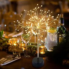 a table topped with wine glasses filled with lights and greenery next to a bottle