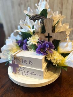 a cross and flowers on a table with the word he is risen