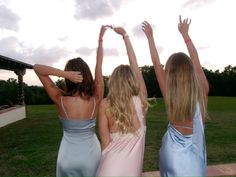 three beautiful young women standing next to each other on top of a lush green field