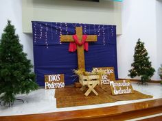 a wooden cross sitting on top of a table next to christmas trees in front of a blue wall