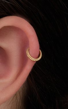 a woman's ear is shown with a small gold hoop in the shape of a crescent