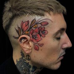 a man with a flower tattoo on his face and behind his ear, looking to the side