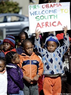 a group of children holding up a sign that reads mrs obama welcome to south africa