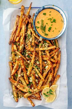 baked french fries with dipping sauce and lemon wedges on a blue tray next to a bowl of dip