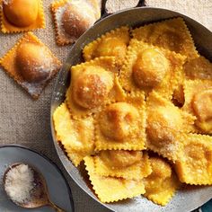 a pan filled with ravioli next to two spoons on top of a table