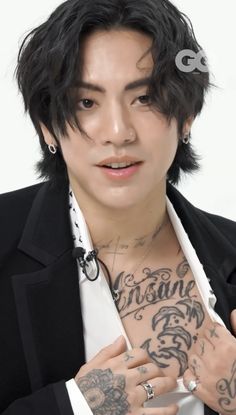 a man with tattoos on his chest wearing a black jacket and white shirt is posing for the camera