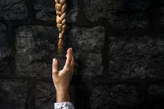 a person's hand reaching up towards a long braid on a black stone wall