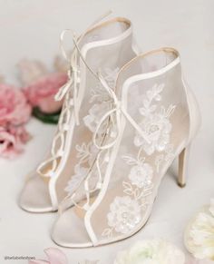 a pair of white high heeled shoes sitting on top of a table next to flowers