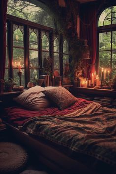 a bed with pillows and blankets in front of two large windows filled with lit candles