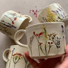 three hand painted mugs with flowers on them are being held in front of the camera