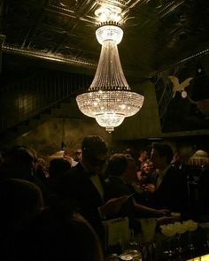 a chandelier hanging from the ceiling in a dark room with people sitting around