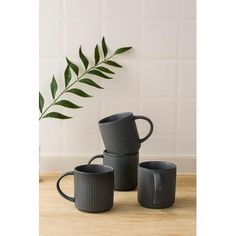 three black mugs sitting on top of a wooden table next to a green plant