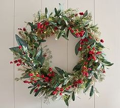 a wreath hanging on the wall with red berries and greenery around it, ready to be hung