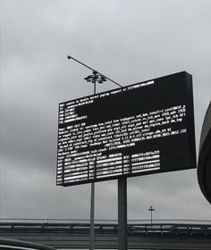 a traffic light sitting next to a large sign on the side of a road in front of an overpass