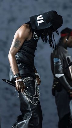 a man with dreadlocks and a black hat walks past another man in leather pants