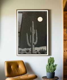 a cactus in a pot next to a chair and a framed poster on the wall