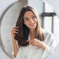 a woman is brushing her hair in front of a mirror and looking at the camera