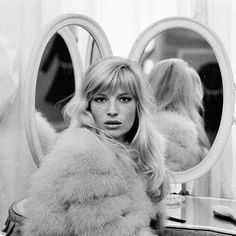 a woman is sitting in front of a mirror with her hair pulled back and wearing a fur coat